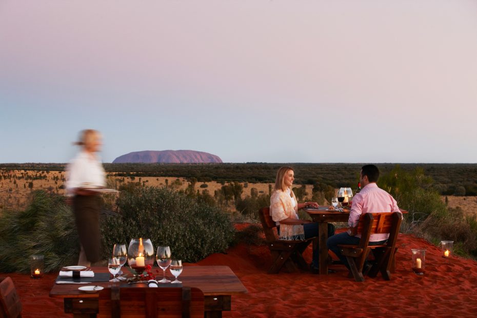 Easting dinner at a table with Uluru in background