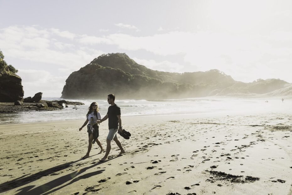 Couple walking on a black sand beach on Auckland's west coast