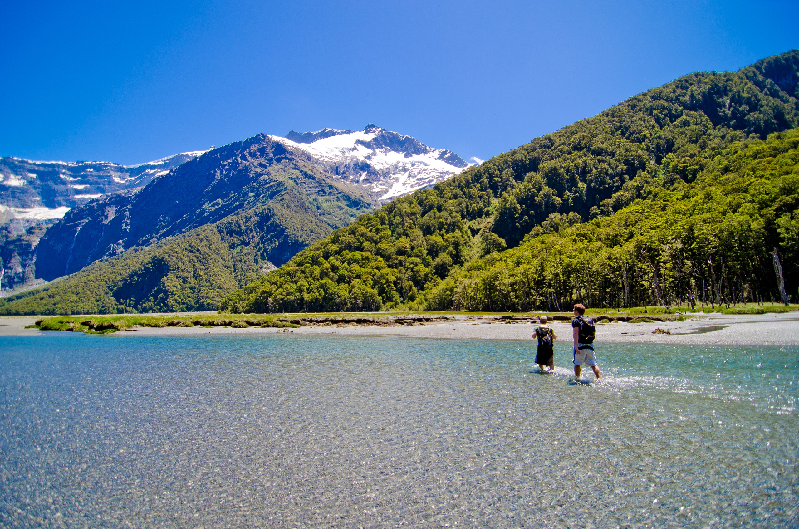 Hikers crossing a river with mountains in the background